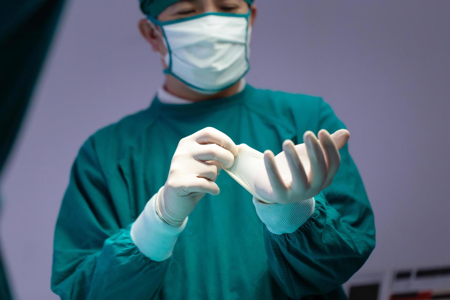 chirurgo maschio che indossa guanti protettivi medici e maschera chirurgica in sala operatoria in ospedale, team medico che esegue operazioni chirurgiche in sala operatoria foto