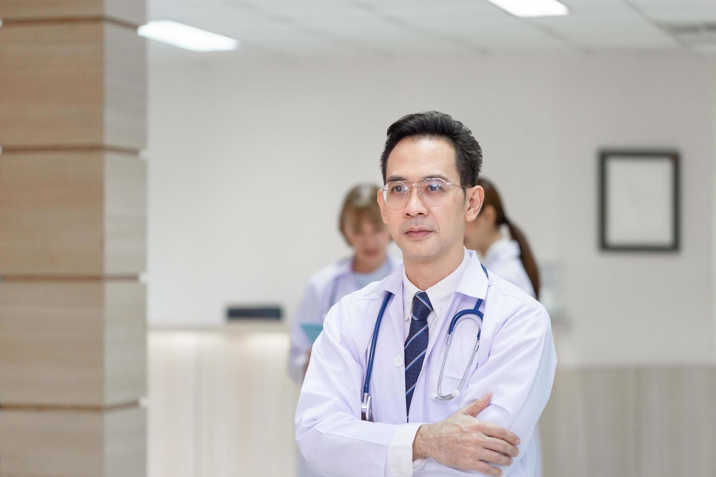 team di medici che sorridono stando in piedi con le braccia incrociate in ospedale, medici in piedi come una squadra con le braccia incrociate foto