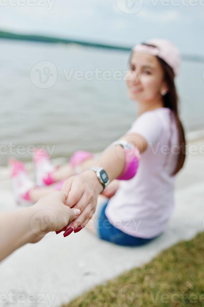 foto ravvicinata di coppia che si tiene per mano mentre è seduto per terra vicino al lago.