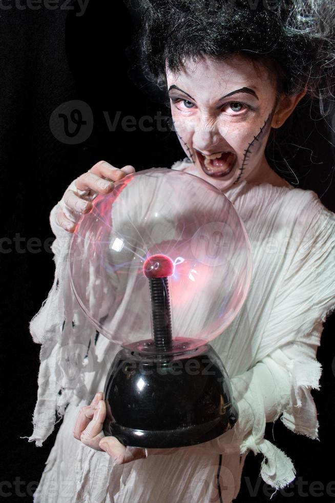 studio shot ritratto di giovane ragazza in costume vestita da halloween, cosplay della spaventosa sposa di frankenstein in posa con una palla di fulmini di vetro foto