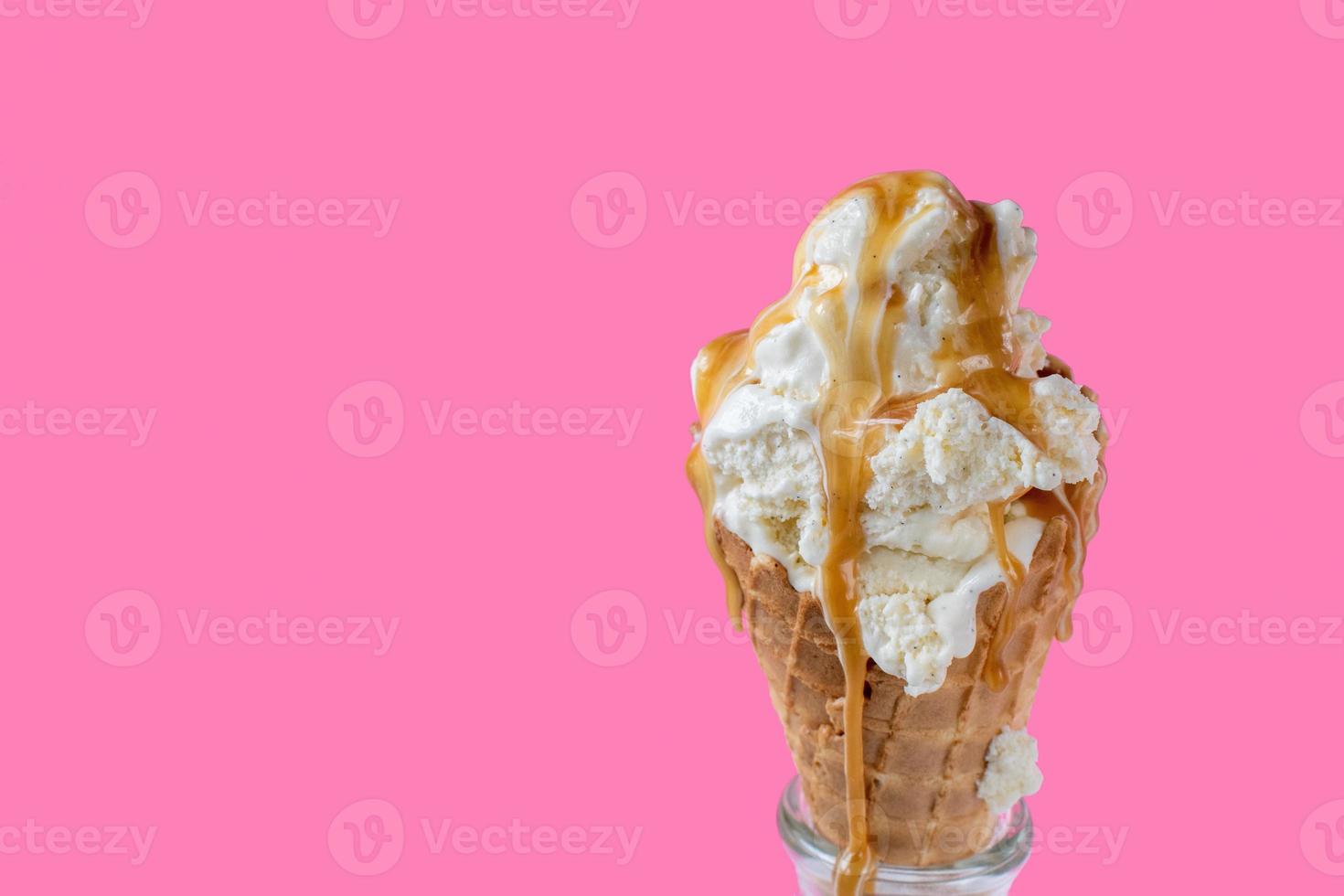 scioglimento di palline di gelato alla vaniglia con salsa al caramello gocciolante su un cono di cialda su uno sfondo rosa vivace e divertente foto