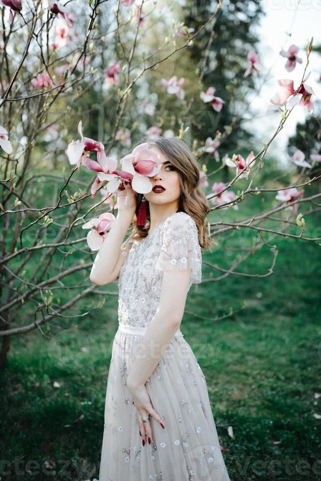 ragazza molto bella la sposa sotto un velo, abito da sposa beige vicino all'albero sakura sta guardando in basso, la natura foto