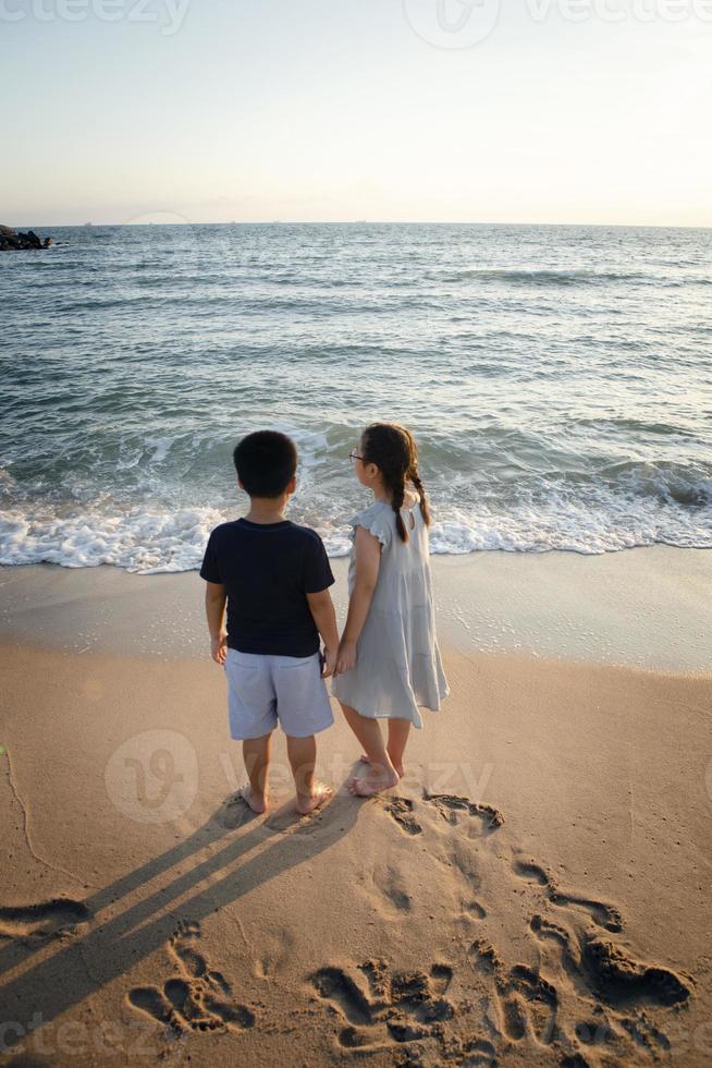 coppie di bambini asiatici in piedi in riva al mare foto