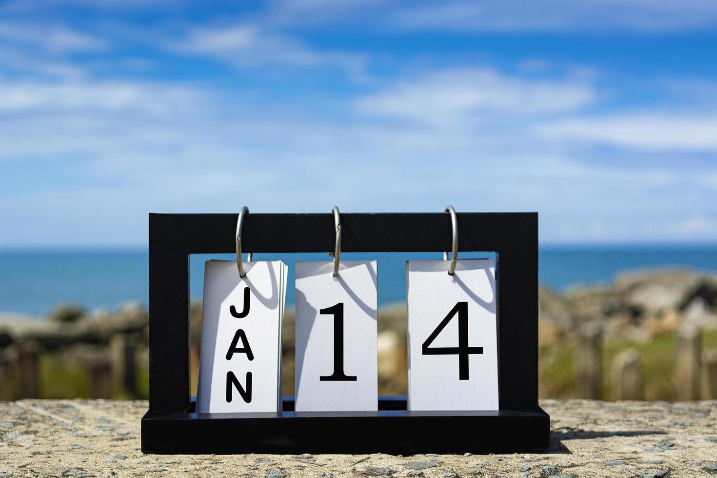 14 gennaio testo della data del calendario su telaio in legno con sfondo sfocato dell'oceano foto