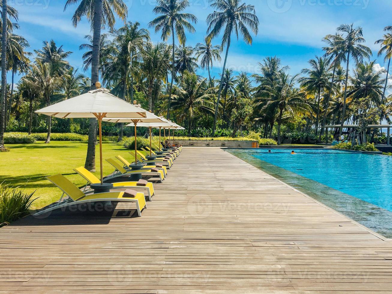 bellissima piscina tropicale in hotel o resort con ombrellone, lettini prendisole con alberi di cocco, palme con vista sulla piscina a sfioro, sfondo dell'oceano e delle montagne. foto