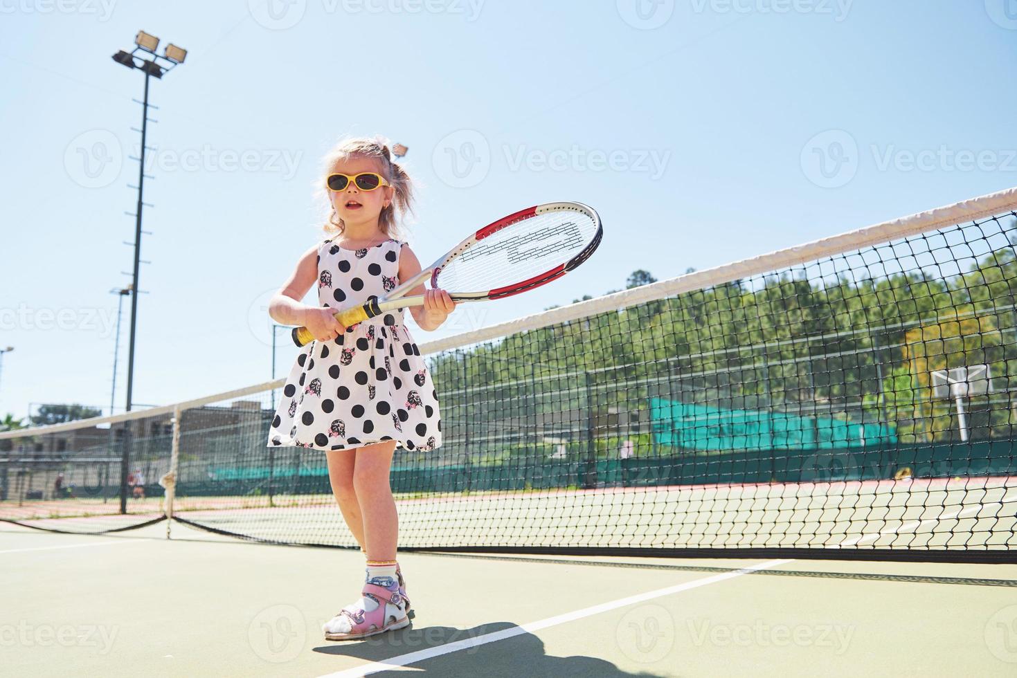 bambina sveglia che gioca a tennis sul campo da tennis all'esterno foto