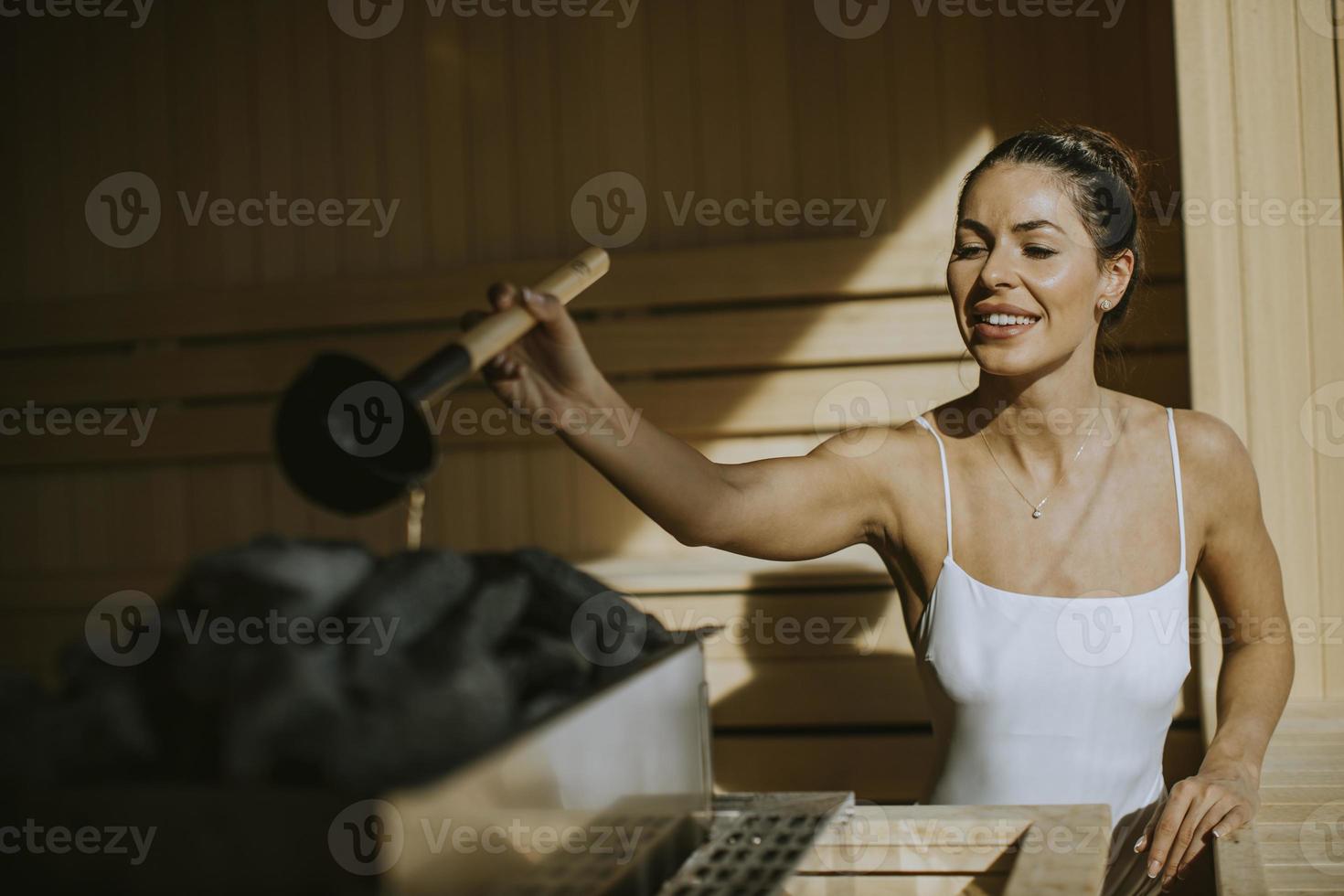 giovane donna che versa acqua sulla pietra calda nella sauna foto