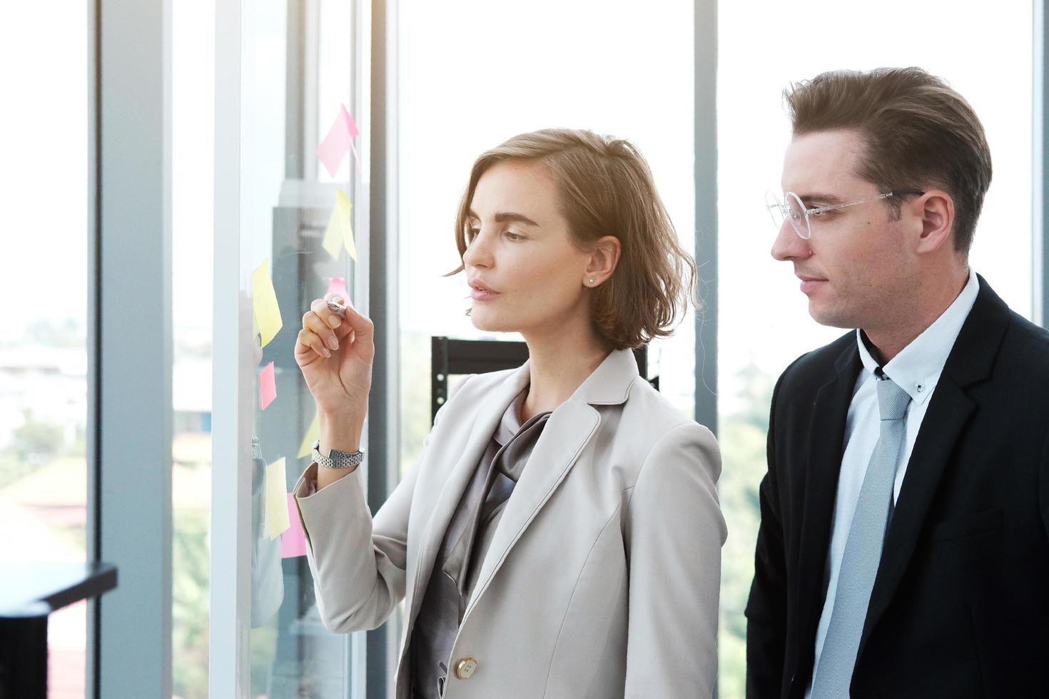 uomo d'affari di successo e donna d'affari che scrivono buone idee su note adesive incollate sulla parete di vetro in una moderna riunione d'ufficio. foto