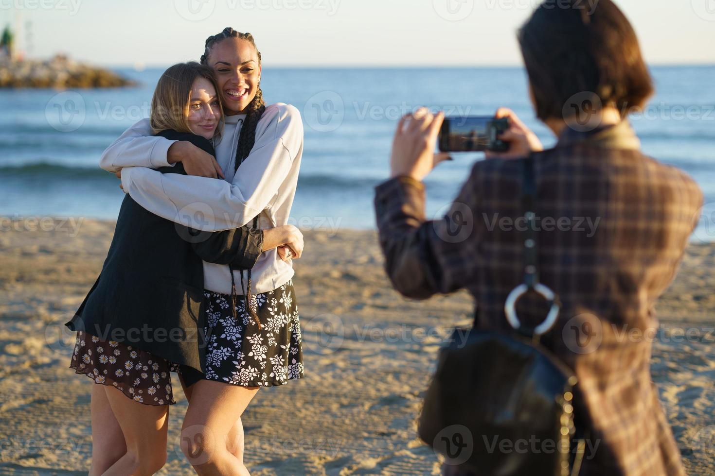 donna senza volto che fotografa diverse amiche positive sulla spiaggia foto