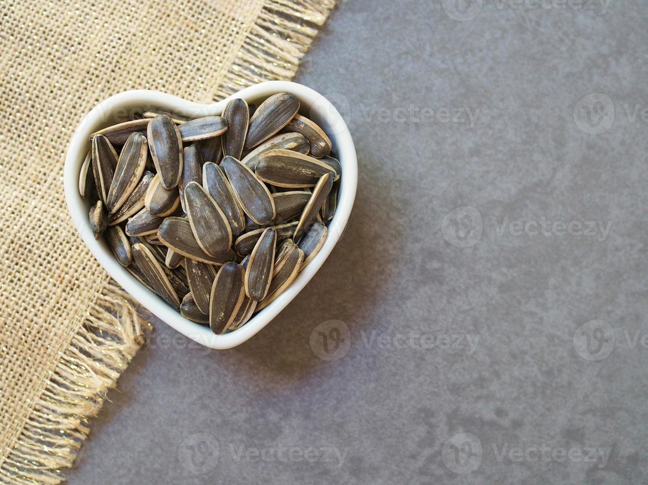 semi di girasole in una tazza bianca a forma di cuore su fondo di cemento. concetto di cibo sano. foto