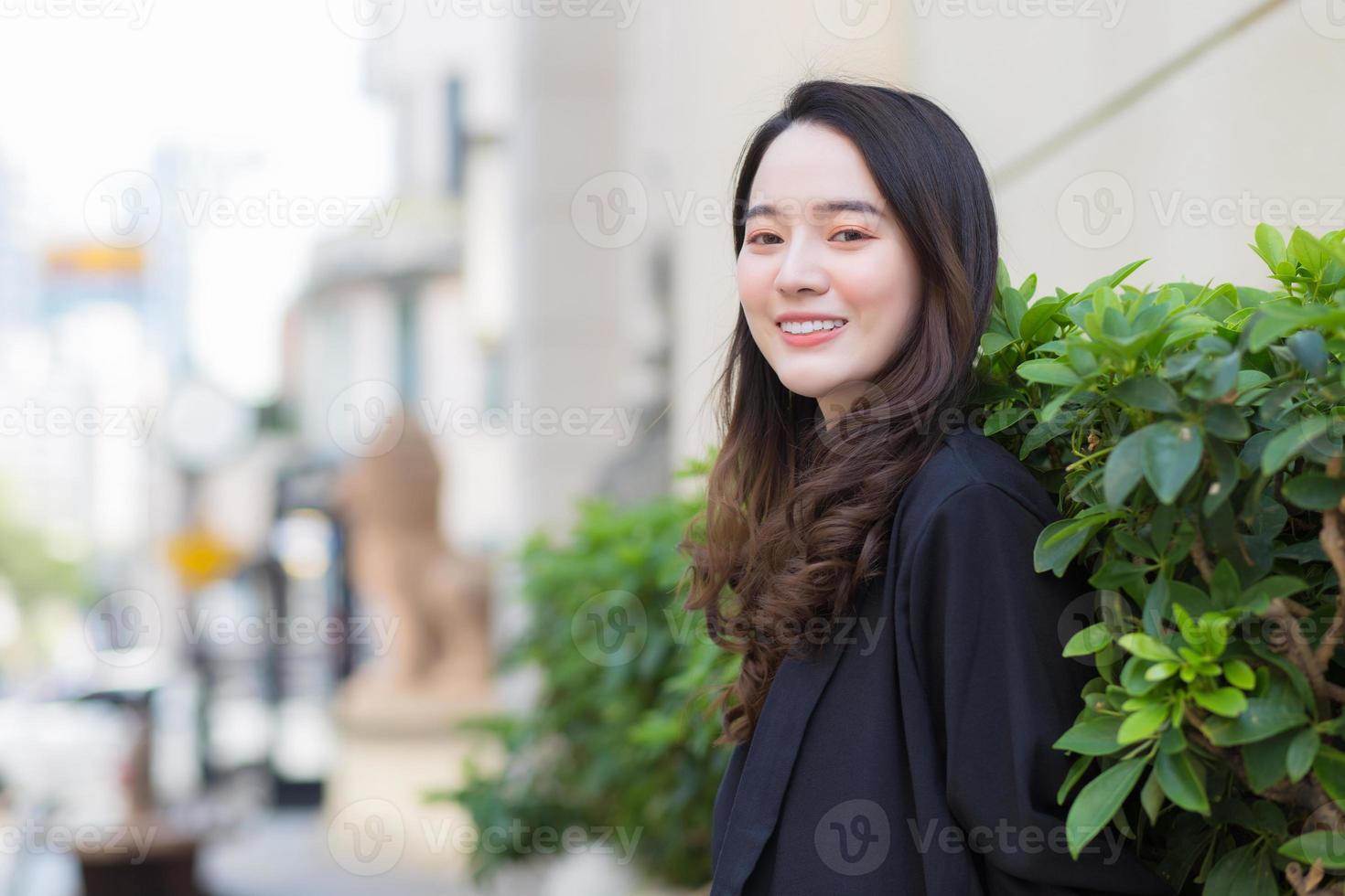 ritratto di bella donna asiatica con i capelli lunghi indossa un cappotto nero in piedi all'aperto in città. foto