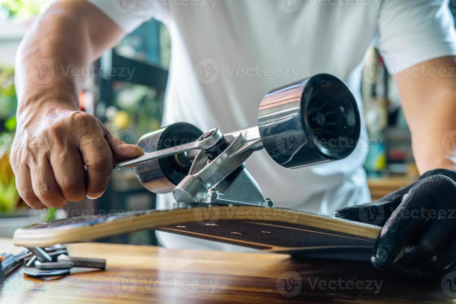 l'uomo usa lo strumento a bussola per rimuovere i dadi sullo skateboard e regola la sospensione in officina, la manutenzione dello skateboard e il concetto di riparazione. messa a fuoco selettiva foto