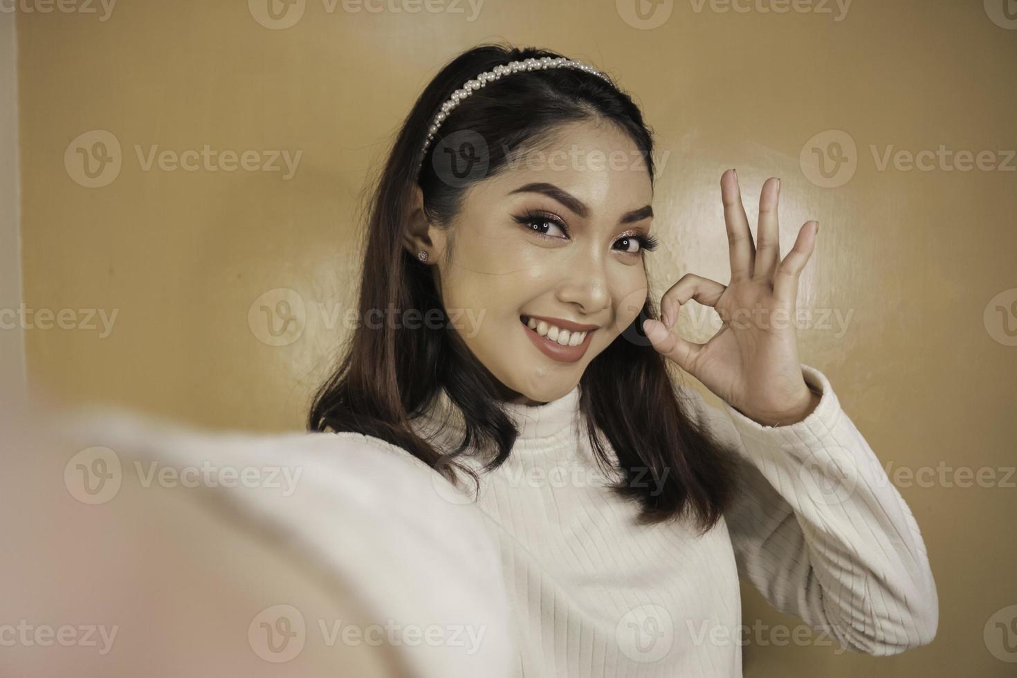 la giovane donna asiatica è selfie con la faccia sorridente felice e il segno giusto vicino alla bocca guarda la telecamera foto