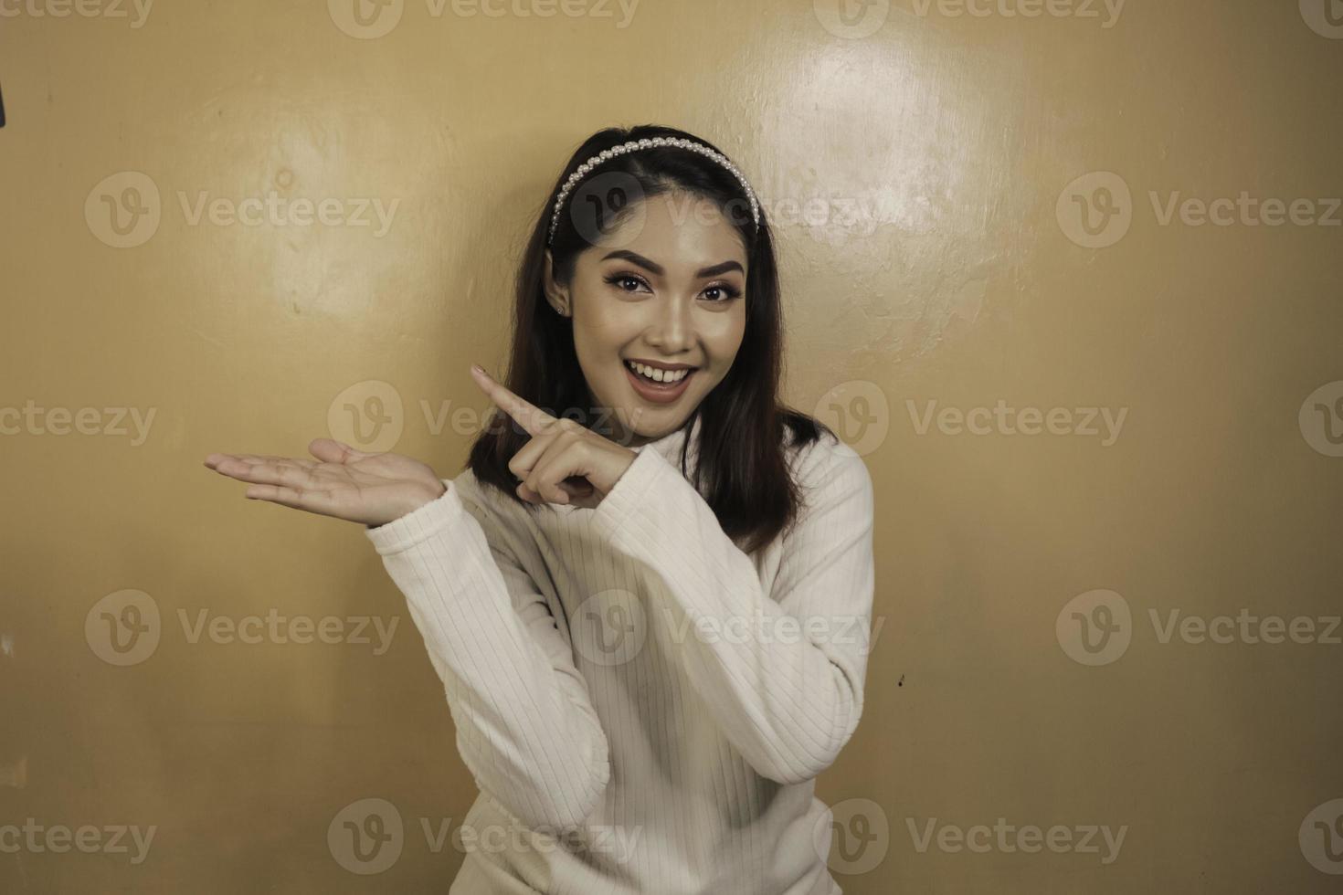 faccia felice e sorridente con il sorriso di una giovane ragazza asiatica con il punto della mano sullo spazio vuoto. foto
