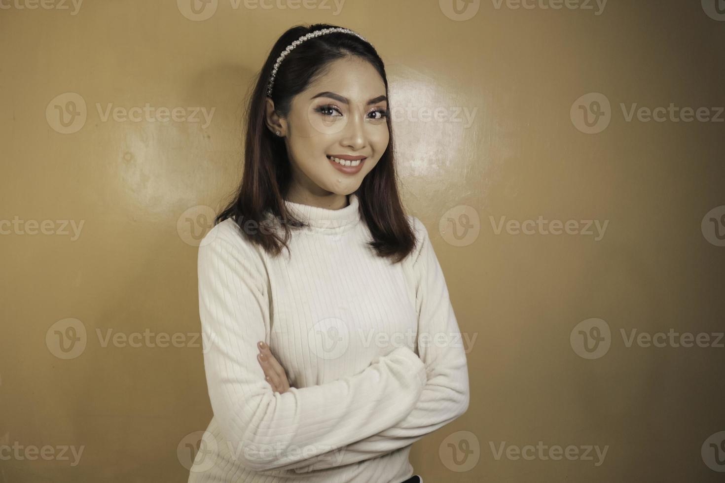 una giovane donna asiatica si tiene per mano incrociata con uno sguardo serio, sorridente e sicuro di sé. foto