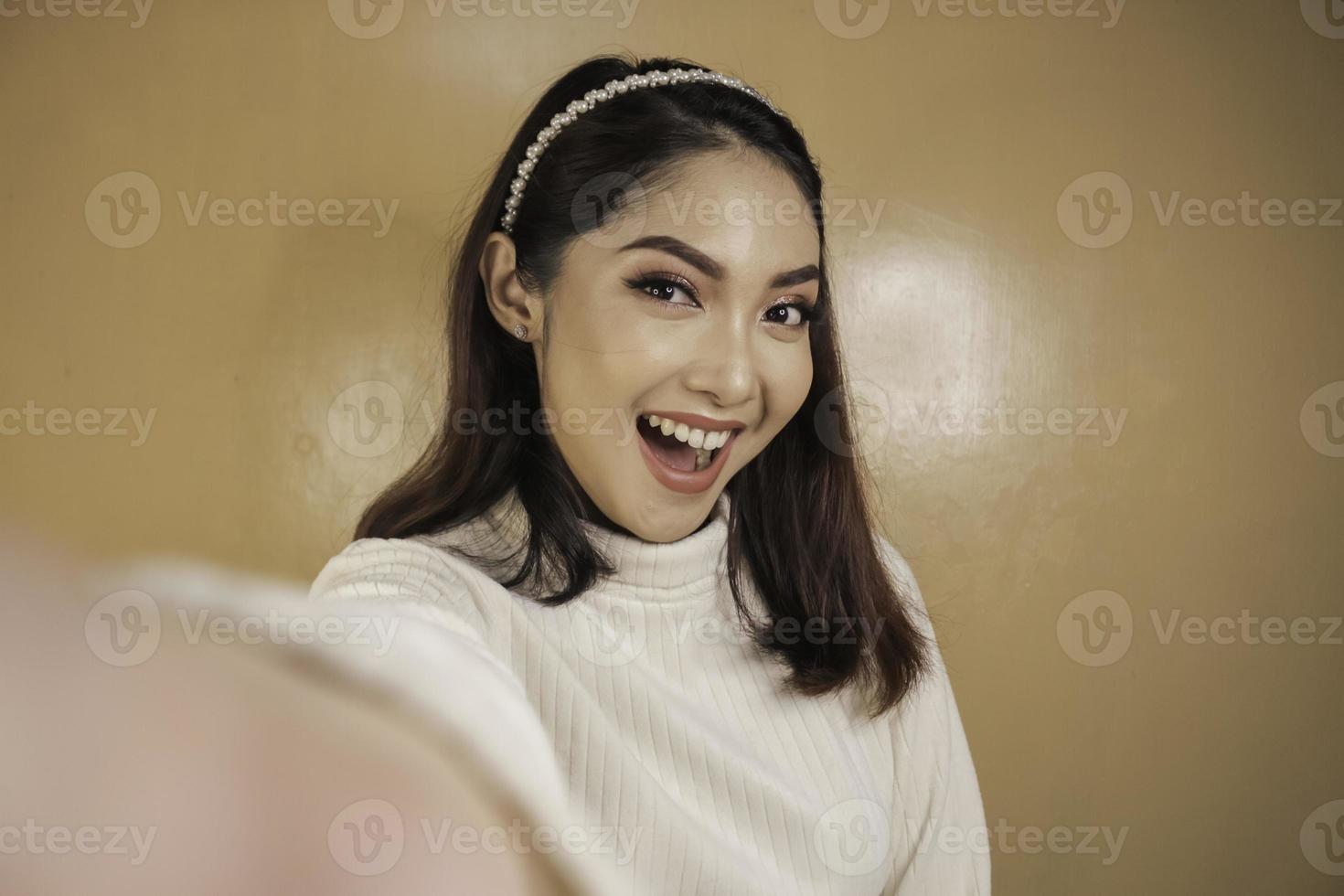 la giovane donna asiatica sta sorridendo e si fa selfie con il suo telefono cellulare. donna indonesiana su sfondo arancione. foto