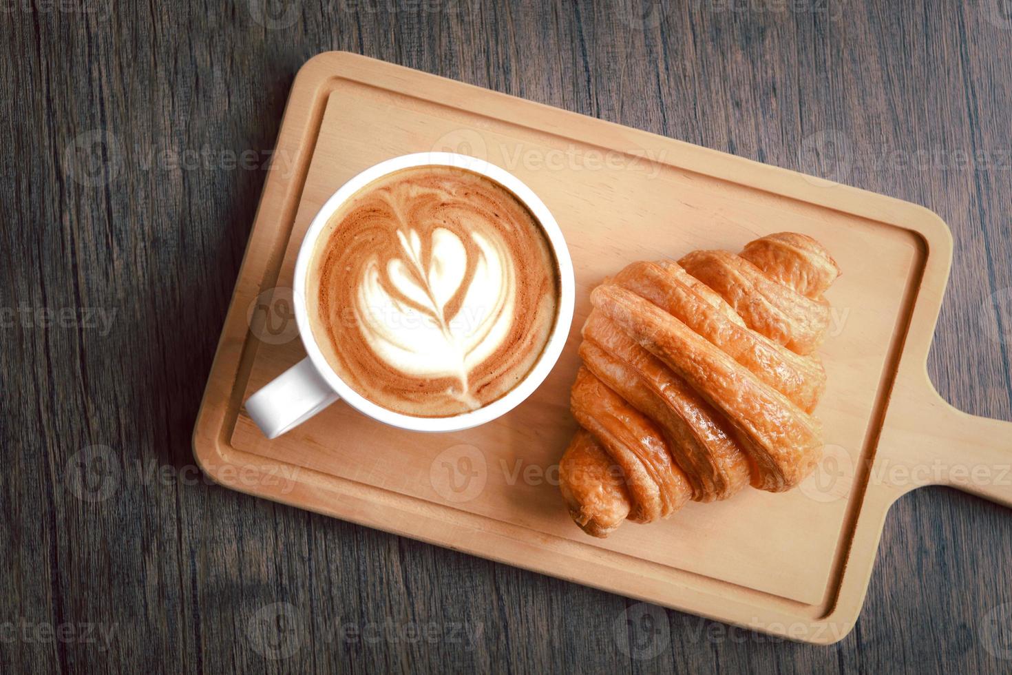 delizioso croissant appena sfornato con una tazza di bel caffè mattutino sul tagliere di legno, vista dall'alto del tavolo per la colazione. foto