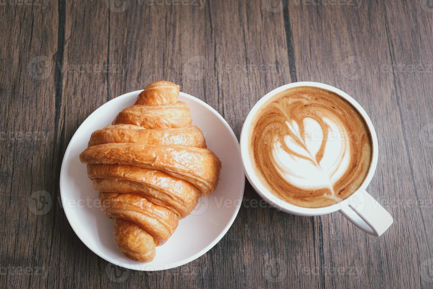 delizioso croissant appena sfornato e tazza di bel caffè mattutino sul tavolo per la colazione in legno, vista dall'alto foto