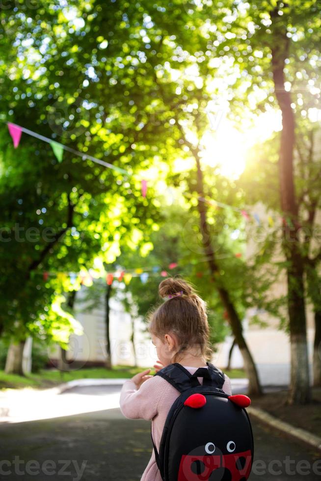 una bambina di razza caucasica in uniforme scolastica con uno zaino guarda la strada nel cortile della scuola. concetto di ritorno a scuola. scuola elementare, sviluppando attività per bambini in età prescolare. spazio per il testo foto