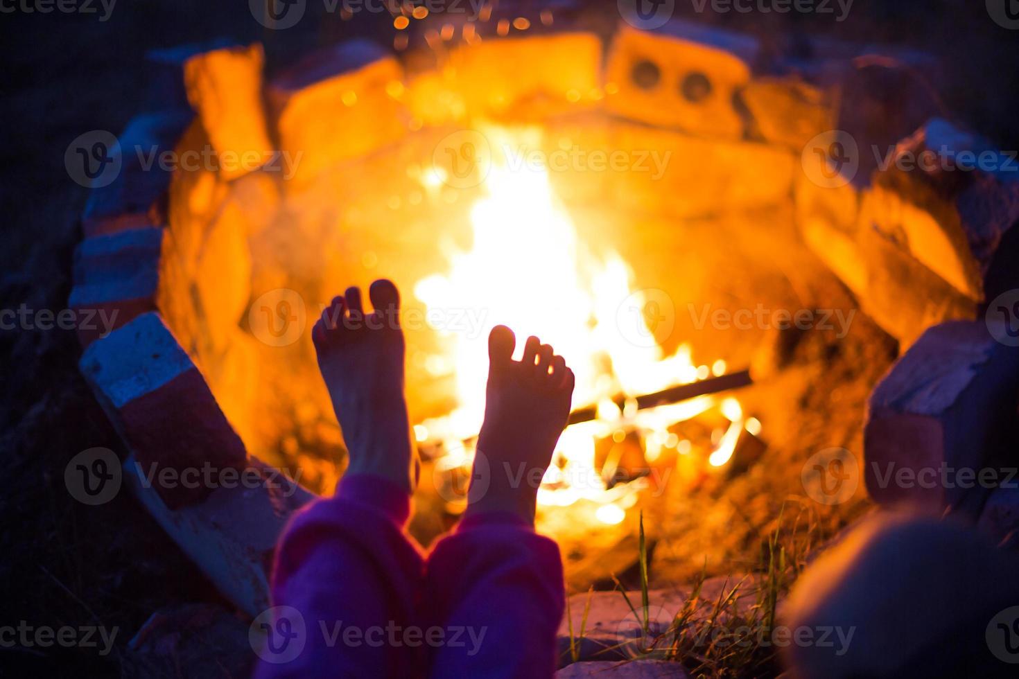 piedi nudi del bambino dal fuoco. incontri notturni al fuoco all'aperto in estate nella natura. campeggio in famiglia, incontri intorno al fuoco. lanterna e tenda da campeggio. scalda i tuoi piedi, notte fredda foto