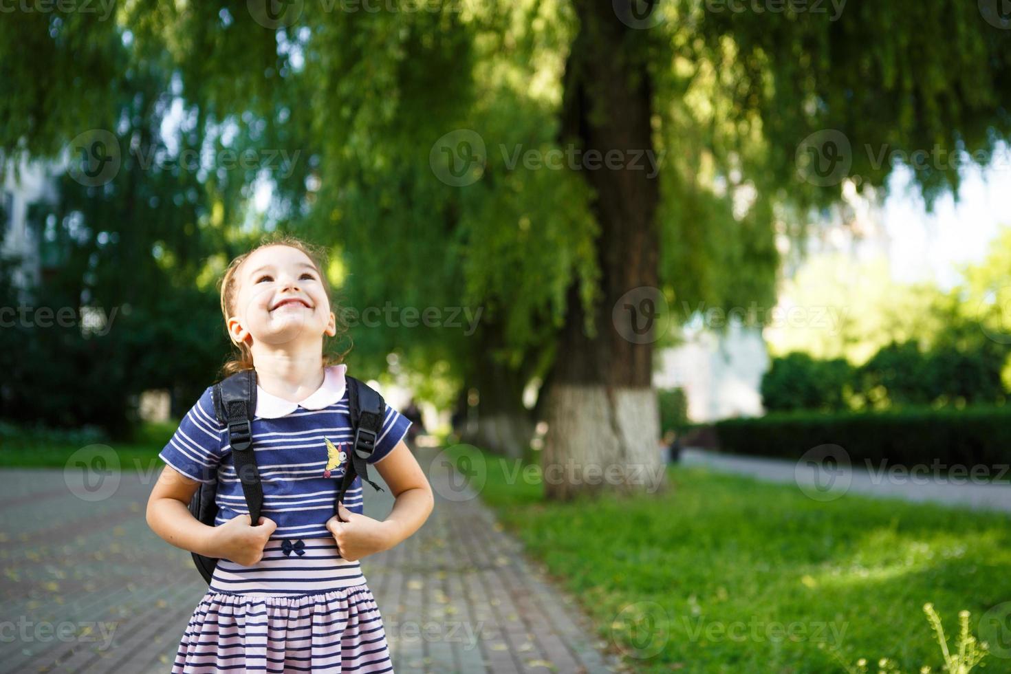 una bambina di aspetto caucasico in uniforme scolastica con uno zaino e il libro. concetto di ritorno a scuola. scuola elementare, sviluppando attività per bambini in età prescolare. spazio per il testo foto