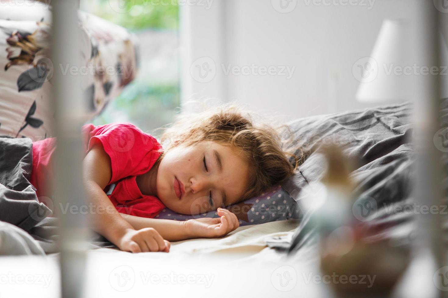 un bambino piccolo dorme dolcemente nel suo letto. sonno sano della ragazza, ventilazione. mattina, sveglia, luce del sole dalla finestra. salita anticipata all'asilo, alla scuola. foto
