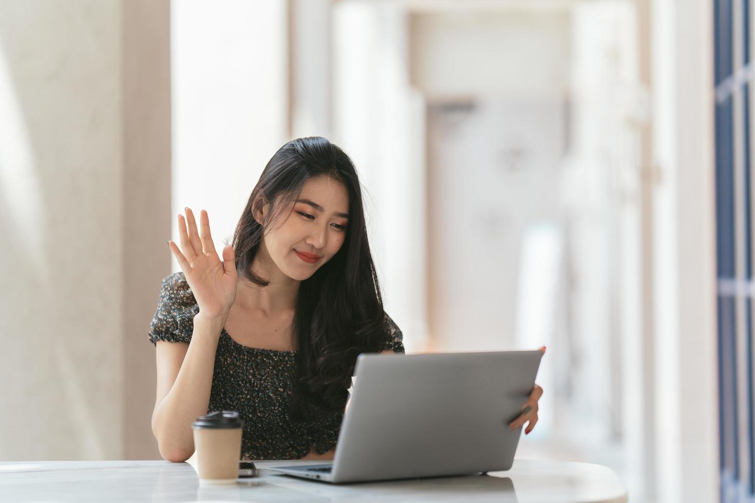 ritratto di giovane donna asiatica che lavora al computer portatile e relazione finanziaria alla caffetteria. foto