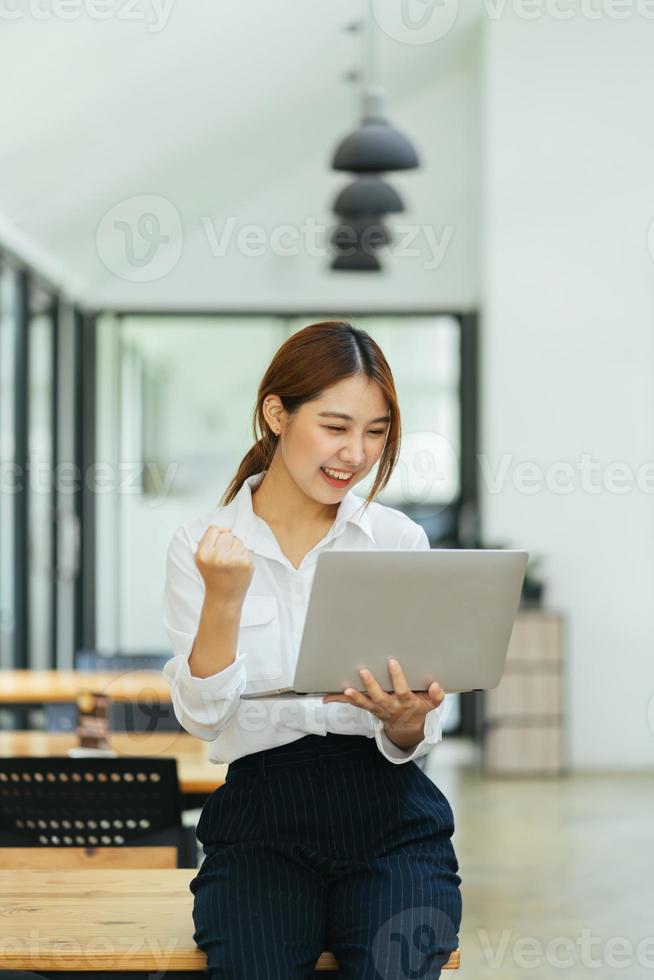 giovane donna con laptop che esprime eccitazione in ufficio a casa, donna asiatica eccitata si sente euforica leggendo buone notizie online. foto