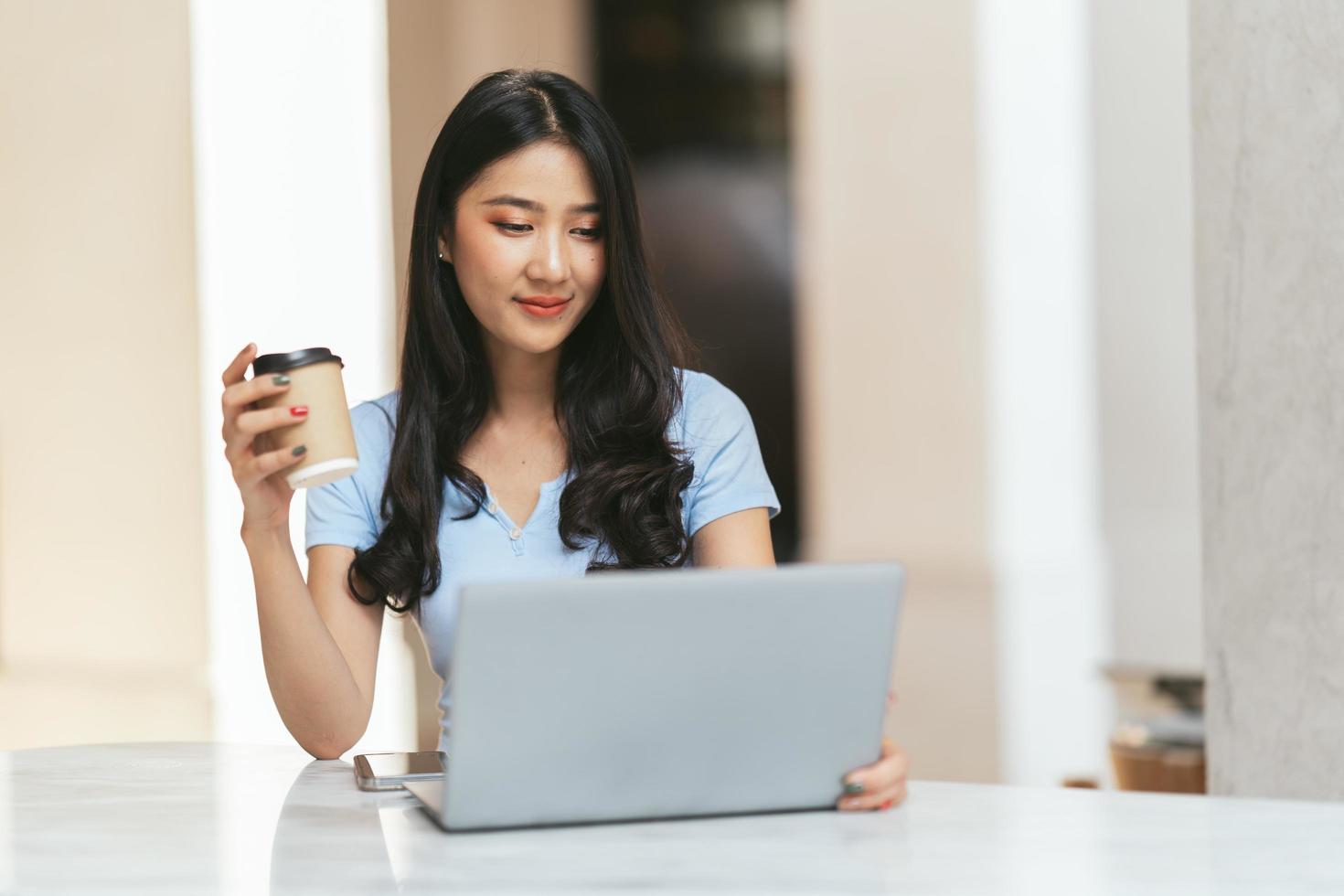 ritratto di giovane donna asiatica che lavora al computer portatile e relazione finanziaria alla caffetteria. foto