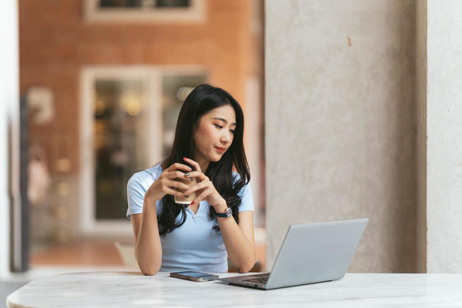 ritratto di giovane donna asiatica che lavora al computer portatile e relazione finanziaria alla caffetteria. foto