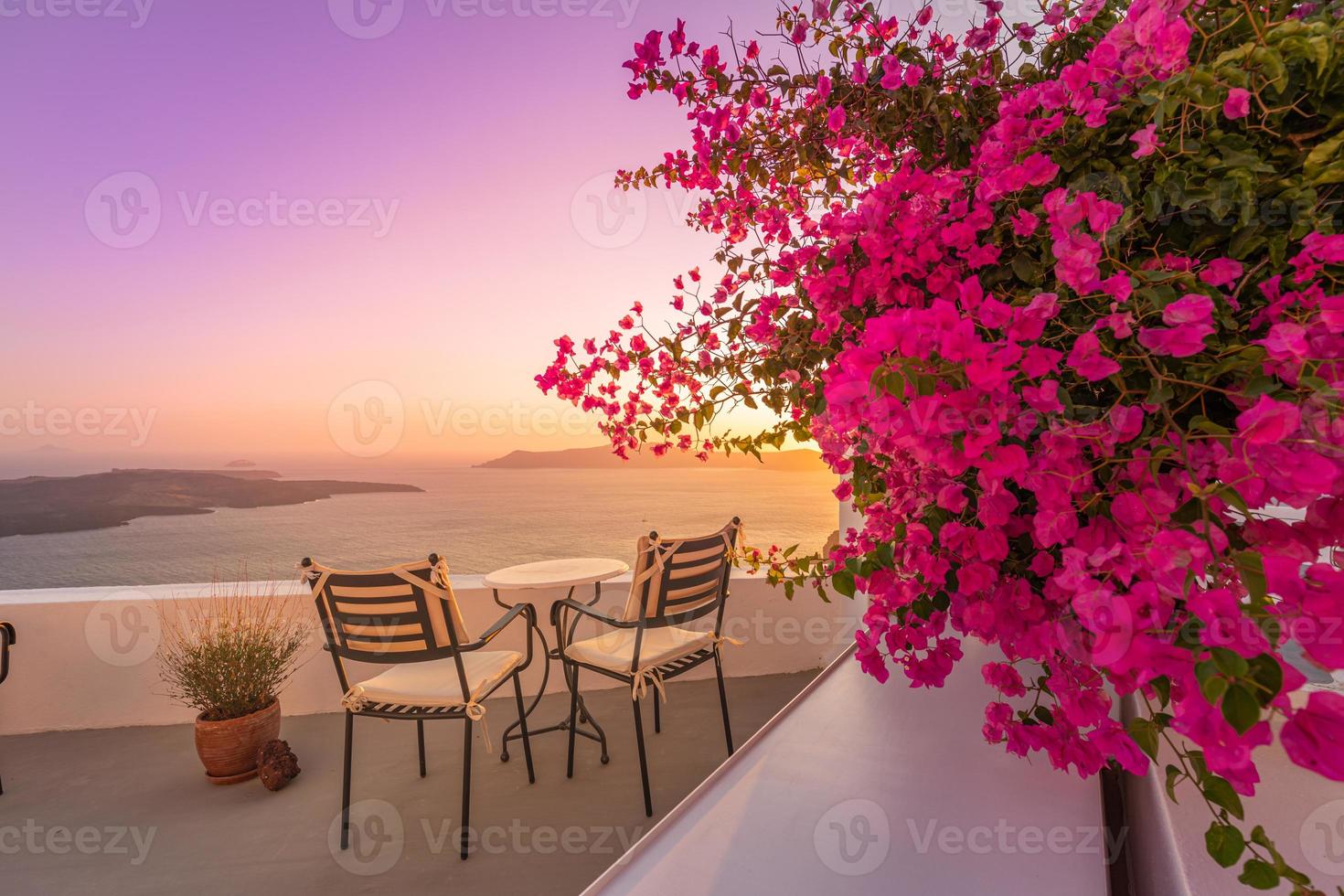 bella vista della caldera e godersi uno scenario romantico tramonto sul mar egeo, santorini. vacanza di viaggio di coppia, destinazione per la luna di miele. romanticismo con fiori, due sedie tavolo e vista mare. vacanza di lusso foto