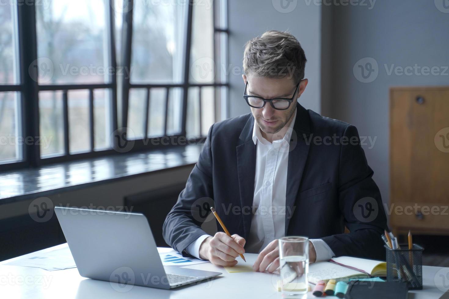 il banchiere maschio concentrato scrive promemoria su note adesive mentre lavora in remoto dall'ufficio di casa foto