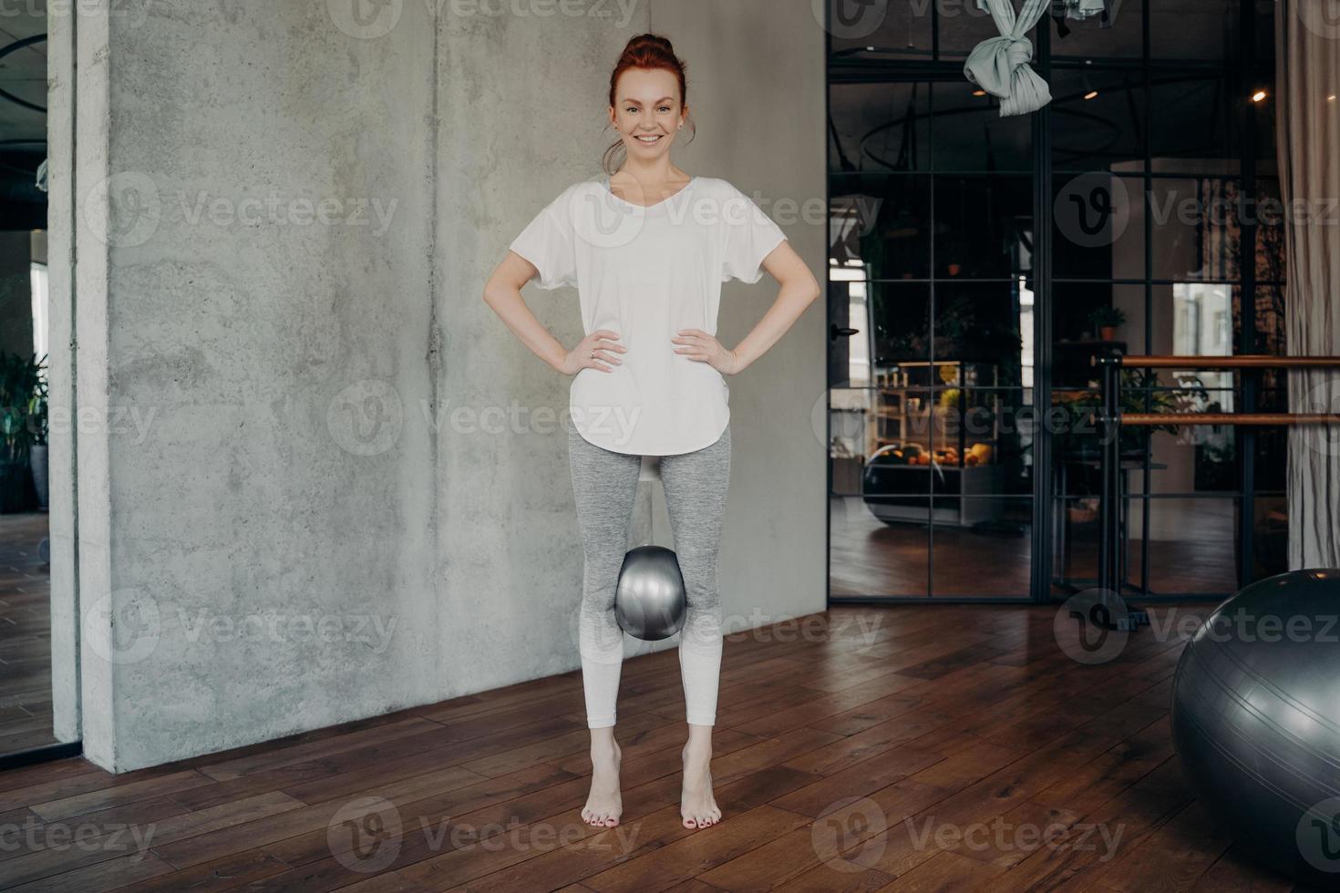 donna rossa sportiva che tiene mini palla pilates con le ginocchia foto