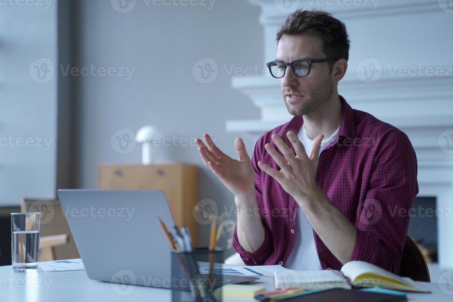 giovane uomo tedesco concentrato con occhiali e abiti casual che partecipa a una riunione virtuale online foto