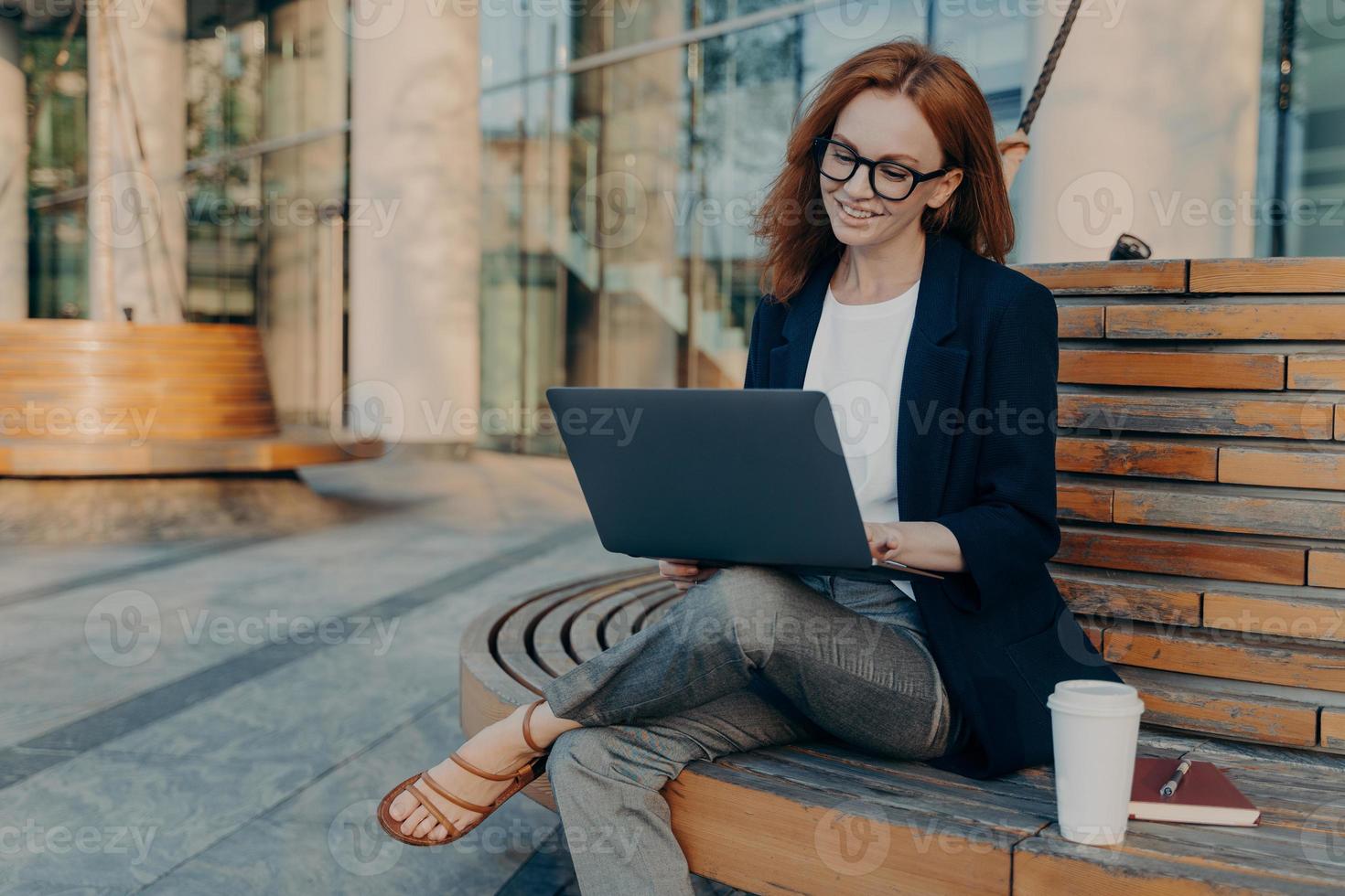 la signora rossa intelligente esplora il laptop all'aperto e fa progetti online foto