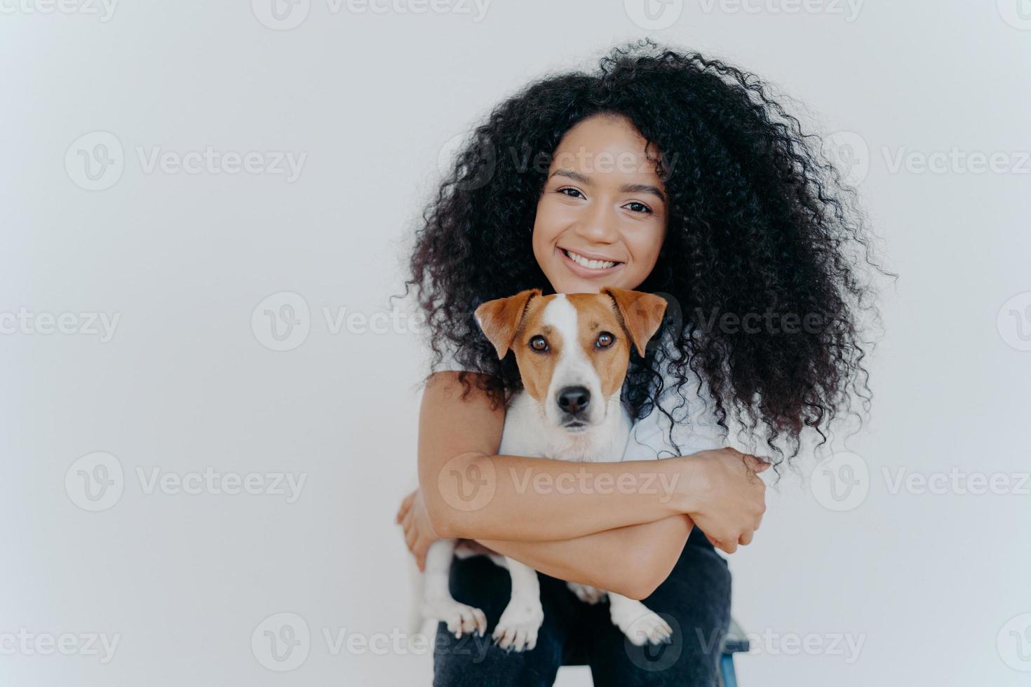 concetto di cura di persone, animali o animali domestici. la donna dai capelli ricci abbraccia il cane preferito, sorride piacevolmente, si trova su uno sfondo bianco, copia l'area dello spazio per i tuoi contenuti pubblicitari. buoni amici. foto