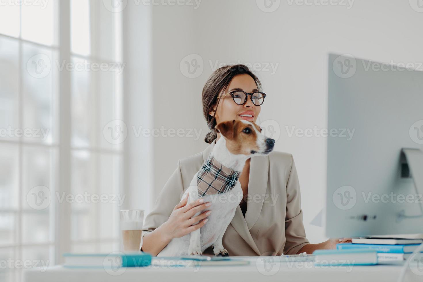 l'insegnante donna impegnata indossa abiti formali e occhiali conduce lezioni online per gli studenti lavora al computer pone nello spazio di coworking con il cane, impegnata a lavorare online. donna d'affari al desktop foto