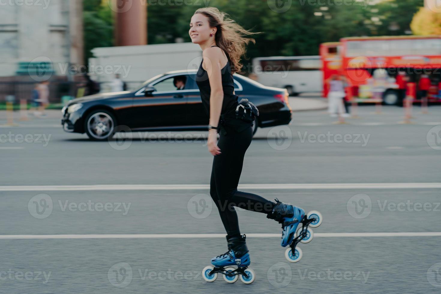 concetto di pattinaggio. la giovane donna in forma attiva va sui pattini lungo una strada trafficata con i mezzi di trasporto ha i capelli che fluttuano nel vento essendo in buona forma fisica si gode il riposo e la ricreazione. foto