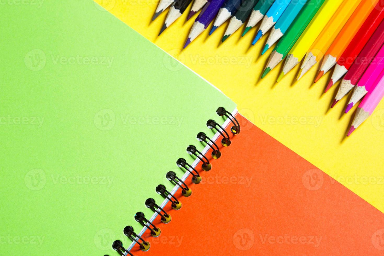 tavolozza arcobaleno di matite colorate con un quaderno a spirale su sfondo giallo, mock up, piatto. ritorno a scuola, reclutamento studenti, artista, lezioni di disegno. copia spazio. cancelleria per la creatività foto