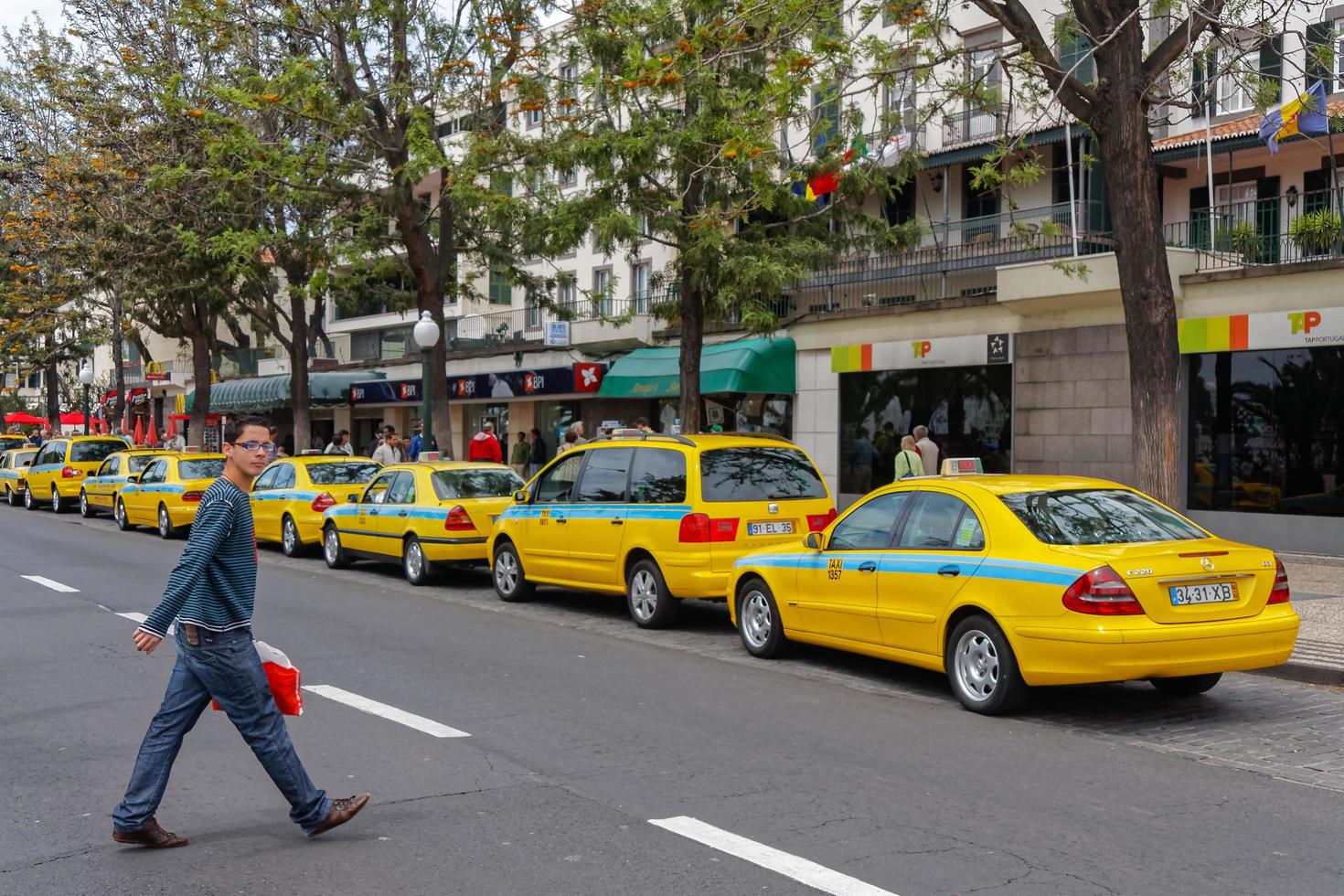 funchal, madera, portogallo, 2008. uomo che cammina attraverso una strada con molti taxi parcheggiati foto