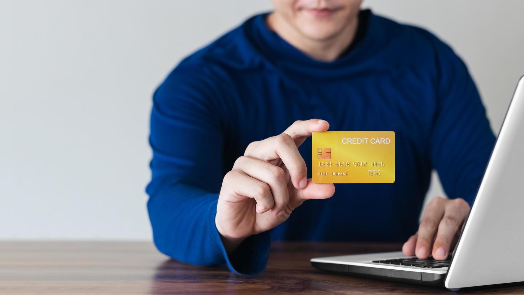 mano dell'uomo d'affari che tiene la carta di credito con l'utilizzo del laptop per lo shopping online mentre si effettuano gli ordini a casa. business, stile di vita, tecnologia, e-commerce, digital banking e concetto di pagamento online. foto