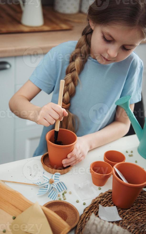 bambina seduta al tavolo di casa, seminando semi in vasi di fiori. foto