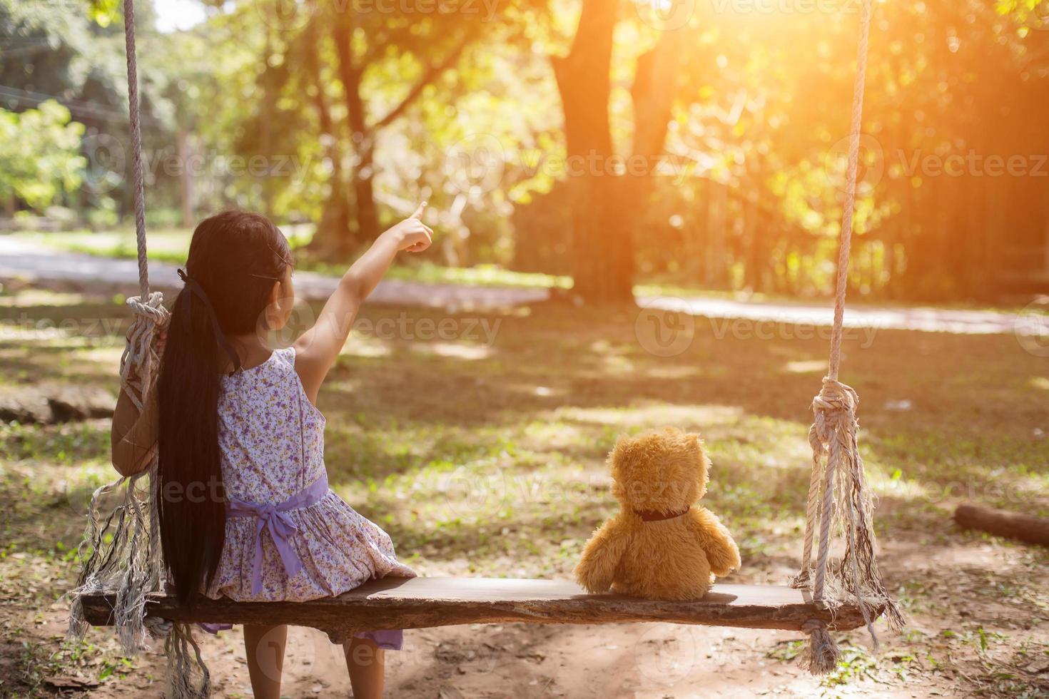 una bambina e un orsacchiotto seduti su un'altalena. foto