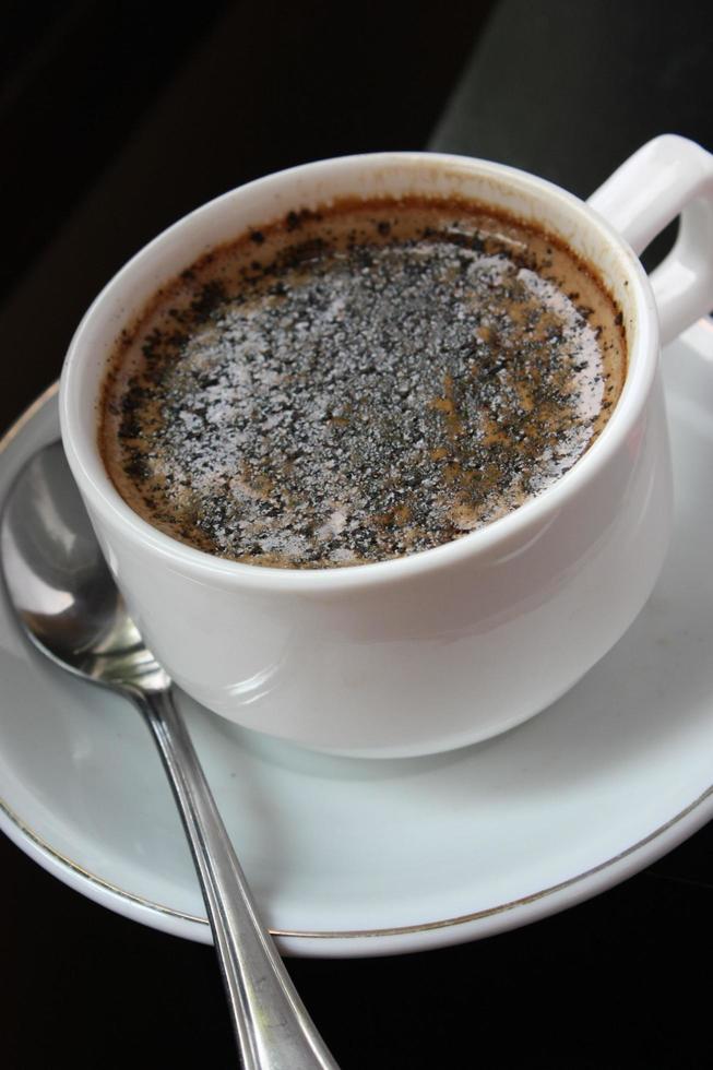 una tazza di caffè espresso con cioccolata calda. con granelli di cioccolato. tazza e piattino bianchi. un cucchiaio inossidabile. sfondo nero. primo piano vista dall'alto. foto