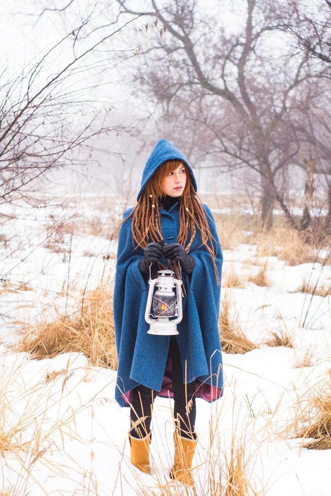 giovane donna in cappotto blu retrò a piedi nel parco nebbioso nei periodi invernali, neve e alberi sullo sfondo, fantasia o concetto di fata foto