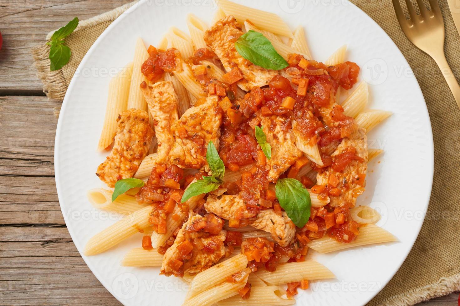 penne, filetto di pollo o tacchino, salsa di pomodoro con foglie di basilico su vecchio fondo di legno rustico. vista dall'alto, primo piano foto