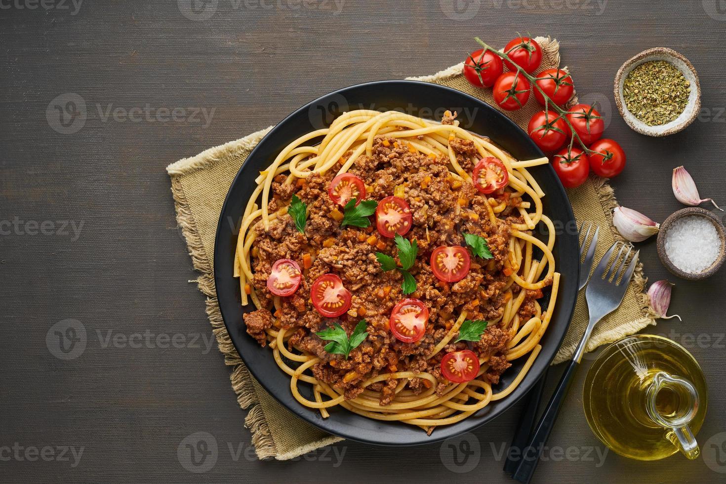 bucatini di pasta alla bolognese con carne macinata e pomodori, fondo in legno scuro, vista dall'alto, spazio per la copia foto