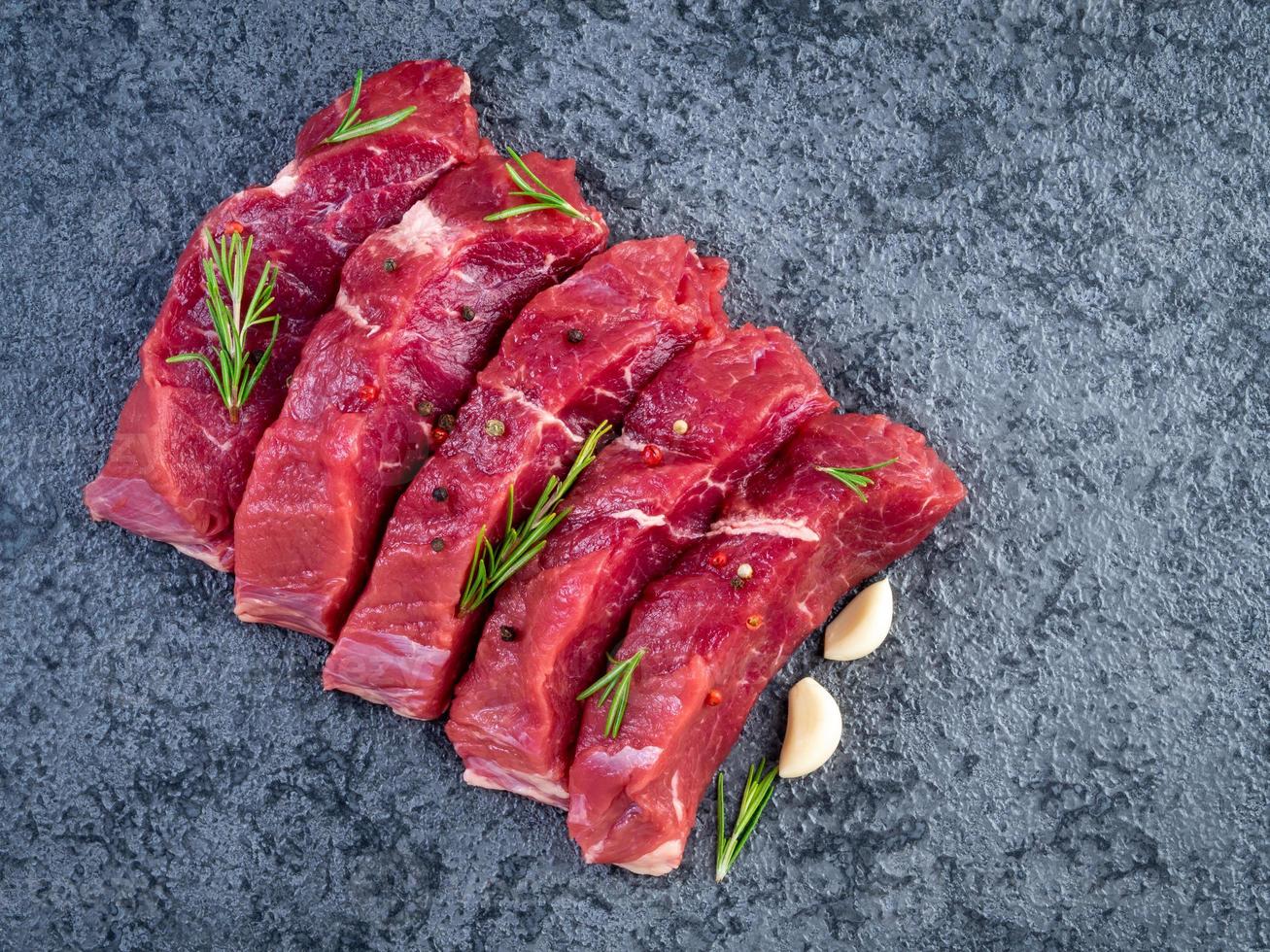 carne cruda, bistecca di manzo con condimento su un tavolo di pietra nera, vista dall'alto foto