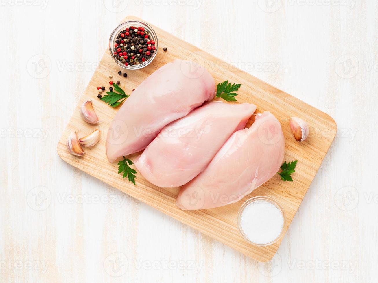 filetto di petto di pollo crudo con spezie su tavola di legno su tavola di legno bianca foto