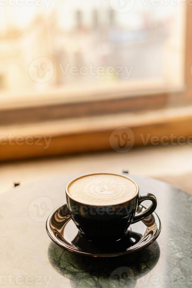 una tazza di cappuccino con schiuma su un tavolo di marmo vicino alla finestra in un piccolo e accogliente caffè. bere con latte vegetale, farina d'avena, cocco foto